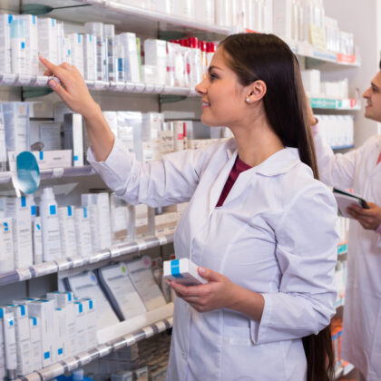 Smiling Pharmacist at Medication Shelf